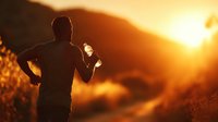 Silhouette of male runner holding water bottle against golden sunset backdrop, mountain trail visible in warm evening light.