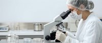 Female scientist in protective gear examining samples through microscope in modern laboratory for medical research and scientific analysis.
