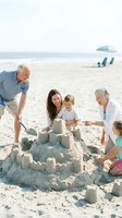 Multi-generational family building sandcastle together on sunny beach, enjoying summer vacation and outdoor recreation activities.