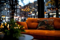 Cozy orange velvet sofa with decorative cushion against blurred evening cityscape background with warm bokeh lights and urban atmosphere.