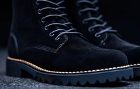 Black suede boots with white laces and chunky rubber sole on dark background, close-up view showing detailed texture and stitching pattern for fashion and footwear design.