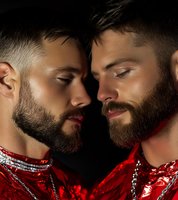 Two bearded men in red metallic clothing face each other intimately against dark background, creating dramatic contrast with glowing skin and fashion styling.