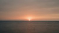 Serene ocean horizon at sunset with golden sun descending over calm waters, creating peaceful atmosphere suitable for wellness, travel, and meditation content.