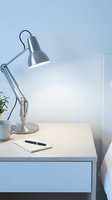 Modern desk lamp with adjustable metal arm and cone shade positioned over white workspace with notebook, pen, and potted plant for office or study lighting solutions.