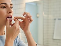 Young woman using dental floss for oral hygiene routine in modern bathroom. Daily teeth cleaning and gum care for healthy smile and dental wellness.