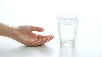 Young adult hand reaching toward glass of fresh water on white surface, isolated on white background for healthcare, wellness, hydration, and medical design use.