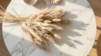 Dried wheat stalks and pampas grass bundle on marble table surface creating natural shadows in warm sunlight for home decor and styling projects.