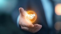Businessman holding glowing handshake icon, symbolizing partnership, agreement, and business cooperation in corporate environment.