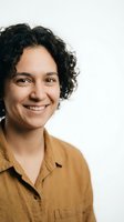 Smiling middle-aged Hispanic woman with curly dark hair wearing mustard yellow shirt against white background for professional headshot photography.