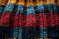 Close up macro shot of striped knitted fabric texture in blue, red and black colors showing detailed wool or cotton yarn pattern and stitches.