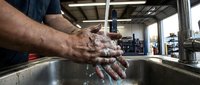Male worker washing hands with soap at industrial sink in manufacturing facility for hygiene safety compliance and contamination prevention.