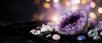 Amethyst geode surrounded by healing crystals and gemstones on dark velvet with golden bokeh lights, spiritual wellness concept.