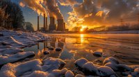 Industrial power plant with smoking chimneys silhouetted against dramatic orange sunset sky, reflected in partially frozen river with snow-covered banks and ice formations.