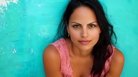 Young Hispanic woman with long dark hair wearing pink top smiling confidently against turquoise wall background, natural beauty and positive expression for lifestyle and portrait concepts.