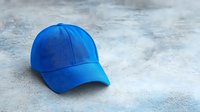 Bright blue baseball cap on textured gray concrete background, clean modern minimalist sports accessory photography for fashion and lifestyle marketing.
