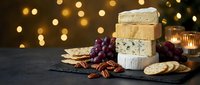Gourmet cheese platter with crackers, grapes and nuts on dark slate board with warm bokeh lights creating elegant appetizer presentation for entertaining.