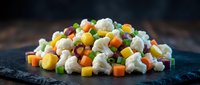 Fresh mixed vegetables including cauliflower, carrots, peas and corn arranged on dark slate surface for healthy cooking and meal preparation.