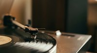 Vintage turntable with tonearm and cartridge playing vinyl record in warm ambient lighting creating nostalgic atmosphere for music lovers and audiophiles.