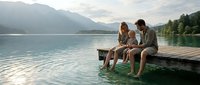 Family enjoying peaceful moment together on wooden dock by mountain lake during golden hour sunset creating serene outdoor lifestyle scene.