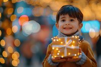 Happy Asian child holding glowing Christmas gift box with magical bokeh lights background, perfect for holiday season advertising and festive family moments.