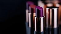 Purple lipstick in metallic tube stands among blurred cosmetic products on dark background, luxury beauty makeup concept for cosmetic advertising.
