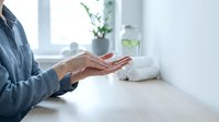 Woman hands in meditation pose on white desk in bright modern office space with plants creating peaceful wellness atmosphere for mindfulness practice.