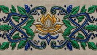 Ornate floral embroidery border with golden rose and blue scrollwork on beige fabric. Traditional decorative needlework pattern for textile design projects.