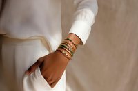 Close-up of woman's wrist adorned with multiple gold bangles and bracelets against white outfit, showcasing elegant jewelry accessories.