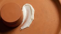 Cream foundation swatch with closed jar on warm terracotta background, showcasing makeup texture and coverage for cosmetic advertising and beauty product promotion.