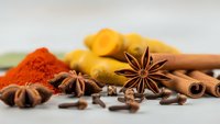 Aromatic spices including star anise, cinnamon sticks, turmeric, paprika and cloves arranged on neutral background for culinary and cooking projects.