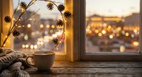 Cozy autumn window scene with coffee cup, pine cone wreath and warm bokeh lights creating peaceful morning atmosphere for seasonal home decor concepts.