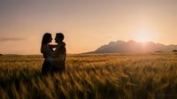 Romantic couple silhouette embracing in golden wheat field at sunset with mountain backdrop, love and connection in nature landscape for wedding concepts.