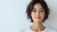 Young Asian woman with short wavy hair and natural makeup wearing white t-shirt smiling confidently against light background. Modern casual portrait for beauty and lifestyle content.