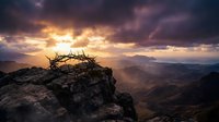 Crown of thorns resting on rocky mountain peak at sunset with dramatic golden light breaking through storm clouds over vast valley landscape.