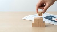 Hand placing wooden block with bicycle icon on pyramid of cubes over documents on desk for eco-friendly transportation and sustainable business concepts.
