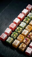 Colorful Turkish delight lokum cubes with nuts and powdered sugar arranged on dark slate background for gourmet dessert and confectionery presentations.