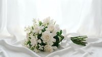White rose bridal bouquet with green foliage on silk fabric background for wedding ceremony and romantic occasions.