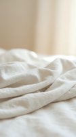 Crumpled white linen fabric with soft folds and natural texture, suitable for home decor, textile design, and bedding product photography.