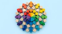Colorful wooden blocks arranged in circular rainbow pattern on light blue background. Natural wood cubes create vibrant mandala design for educational toys and creativity.