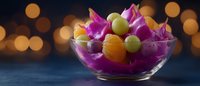 Fresh fruit salad with dragon fruit, grapes and mandarin oranges in glass bowl against dark background with golden bokeh lights creating festive mood.