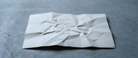 Crumpled white paper sheet with wrinkles and creases on dark surface, representing failure, mistakes, discarded ideas or starting over concepts.