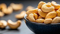 Fresh roasted cashew nuts in dark ceramic bowl against black background, selective focus on golden nuts with natural lighting and blurred foreground.