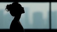 Silhouette of woman against window with urban skyline backdrop, conveying solitude and contemplation in modern city environment.