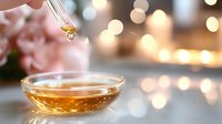 Golden drop of essential oil falling from glass dropper into bowl with aromatherapy oil against blurred warm bokeh lights and roses background. Spa and wellness concept.