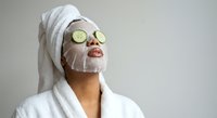 Young woman enjoying spa treatment with cucumber slices on eyes and facial mask wearing white bathrobe and towel for skincare and wellness routine.
