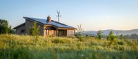 Modern eco-friendly house with solar panels in rural meadow landscape at golden hour sunset, sustainable living and renewable energy concept.