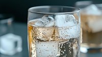 Refreshing cold drink with ice cubes and bubbles in clear glass against dark background, macro shot showing carbonation and condensation details.