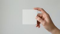 Caucasian male hand holding blank white square card or paper against neutral gray background for branding, mockup, or presentation purposes.