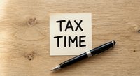 Tax time reminder note with black pen on wooden desk surface for accounting and financial planning preparation.