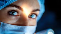 Close up portrait of female medical professional with intense blue eyes wearing surgical mask and cap against dark background, dramatic lighting highlights gaze.